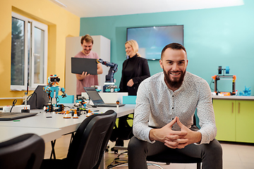 Image showing A man sitting in a robotics laboratory while his colleagues in the background test new, cutting edge robotic inventions.