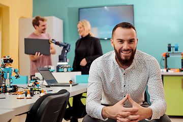 Image showing A man sitting in a robotics laboratory while his colleagues in the background test new, cutting edge robotic inventions.