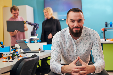 Image showing A man sitting in a robotics laboratory while his colleagues in the background test new, cutting edge robotic inventions.