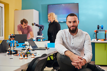 Image showing A man sitting in a robotics laboratory while his colleagues in the background test new, cutting edge robotic inventions.
