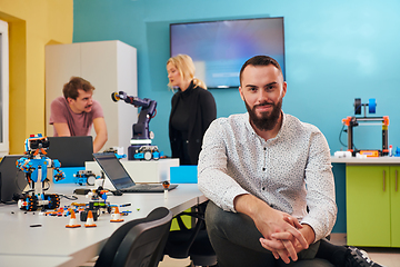 Image showing A man sitting in a robotics laboratory while his colleagues in the background test new, cutting edge robotic inventions.