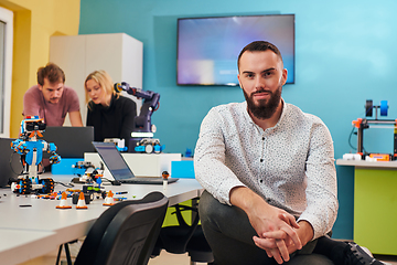 Image showing A man sitting in a robotics laboratory while his colleagues in the background test new, cutting edge robotic inventions.