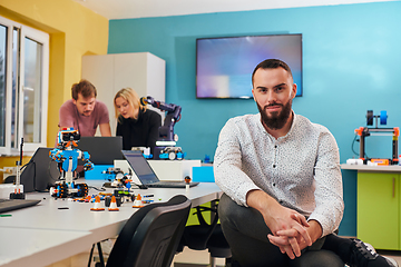 Image showing A man sitting in a robotics laboratory while his colleagues in the background test new, cutting edge robotic inventions.