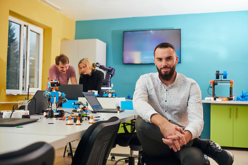 Image showing A man sitting in a robotics laboratory while his colleagues in the background test new, cutting edge robotic inventions.