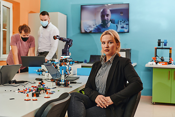 Image showing A woman sitting in a laboratory and solving problems and analyzing the robot's verification. In the background, colleagues are talking at an online meeting