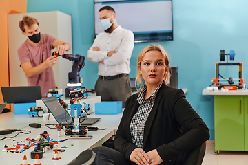 Image showing A woman sitting in a laboratory and solving problems and analyzing the robot's verification. In the background, colleagues are talking at an online meeting