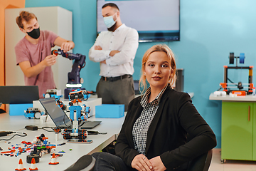 Image showing A woman sitting in a laboratory and solving problems and analyzing the robot's verification. In the background, colleagues are talking at an online meeting