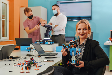 Image showing A woman sitting in a laboratory and solving problems and analyzing the robot's verification. In the background, colleagues are talking at an online meeting