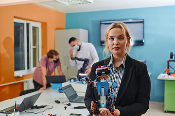 Image showing A woman sitting in a laboratory and solving problems and analyzing the robot's verification. In the background, colleagues are talking at an online meeting