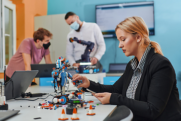 Image showing A woman sitting in a laboratory and solving problems and analyzing the robot's verification. In the background, colleagues are talking at an online meeting