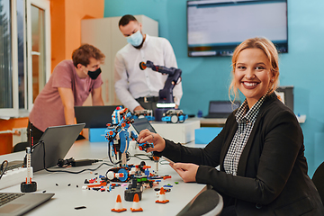 Image showing A woman sitting in a laboratory and solving problems and analyzing the robot's verification. In the background, colleagues are talking at an online meeting