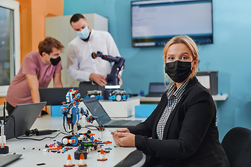 Image showing A woman wearing a protective mask standing in a laboratory while her colleagues test a new robotic invention in the background.