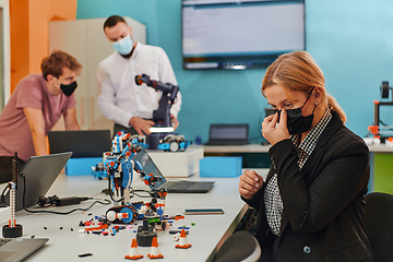 Image showing A woman wearing a protective mask standing in a laboratory while her colleagues test a new robotic invention in the background.