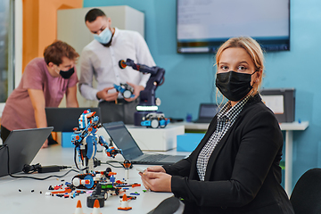 Image showing A woman wearing a protective mask standing in a laboratory while her colleagues test a new robotic invention in the background.