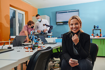 Image showing A woman sitting in a laboratory and solving problems and analyzing the robot's verification. In the background, colleagues are talking at an online meeting