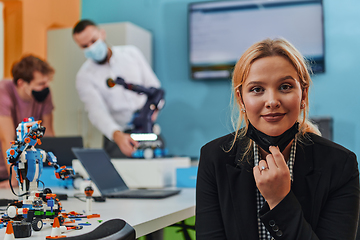 Image showing A woman wearing a protective mask standing in a laboratory while her colleagues test a new robotic invention in the background.