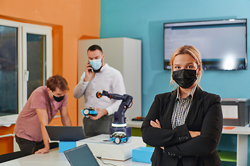 Image showing A woman wearing a protective mask standing in a laboratory while her colleagues test a new robotic invention in the background.