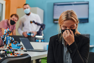 Image showing A woman wearing a protective mask standing in a laboratory while her colleagues test a new robotic invention in the background.