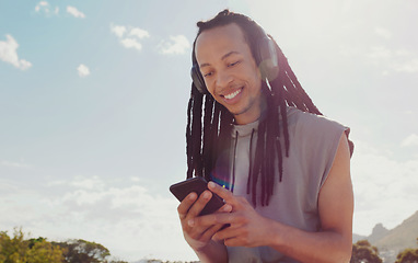 Image showing Sky, black man and smartphone with headphones streaming music, online reading and podcast outdoor. African American male, guy and cellphone for social media, headset and listen to audio and sounds