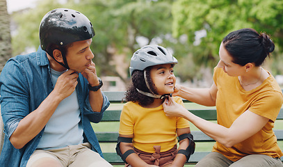 Image showing Parents, park bench and helmet with child, helping hand and safety for skating, rollerskate or bike. Interracial parents, mom and dad with help, teaching and kid for bonding, learning and exercise