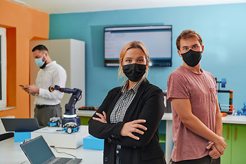 Image showing A woman wearing a protective mask standing in a laboratory while her colleagues test a new robotic invention in the background.