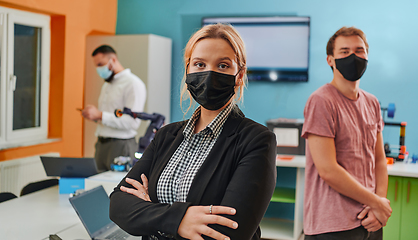 Image showing A woman wearing a protective mask standing in a laboratory while her colleagues test a new robotic invention in the background.