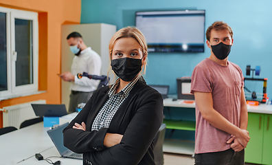 Image showing A woman wearing a protective mask standing in a laboratory while her colleagues test a new robotic invention in the background.