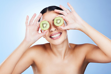 Image showing Beauty, skincare and kiwi on eyes of woman feeling silly from fruit, wellness and vitamin c health. isolated, blue background and smile in studio of a young model happy about green cosmetic treatment