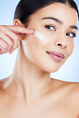 Image showing Woman, face and apply skincare moisturizer in cosmetics or beauty against a blue studio background. Female applying product, lotion or cream for facial treatment, collagen or healthy self care skin