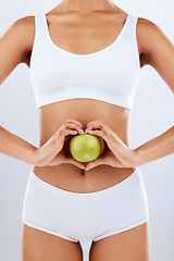 Image showing Nutrition, apple and woman hands on stomach in heart shape for digestion, detox diet and studio background. Fruits, wellness and healthy abdomen body with care, love and lose weight for strong gut
