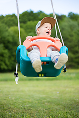 Image showing Adorable little happy Caucasian infant baby boy child swinging on playground outdoors.