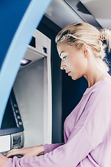 Image showing Young lady withdrawing money at ATM machine entering her pin code.