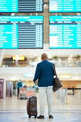 Image showing Black man in airport, flight schedule display and waiting in terminal for international business trip from back. Visa, travel and luggage, businessman checking international destination boarding time