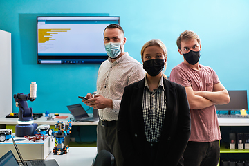 Image showing A group of colleagues stand ingin a robotics laboratory, arms crossed, wearing protective masks, symbolizing their teamwork and commitment to technological innovation and scientific research.