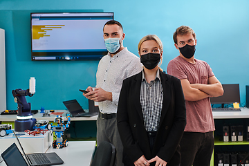 Image showing A group of colleagues stand ingin a robotics laboratory, arms crossed, wearing protective masks, symbolizing their teamwork and commitment to technological innovation and scientific research.