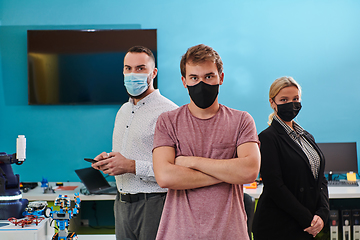 Image showing A group of colleagues stand ingin a robotics laboratory, arms crossed, wearing protective masks, symbolizing their teamwork and commitment to technological innovation and scientific research.