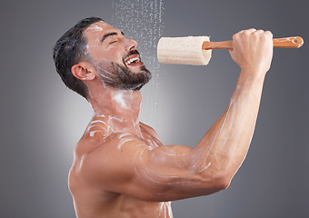 Image showing Shower, cleaning and man singing with brush in studio for skincare, washing body and wellness on gray background. Beauty, bathroom and happy male do karaoke with loofah sponge, soap and water splash