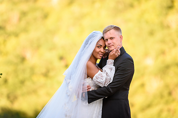 Image showing Happy newlyweds against the background of evening sunny foliage, the couple looks into the frame