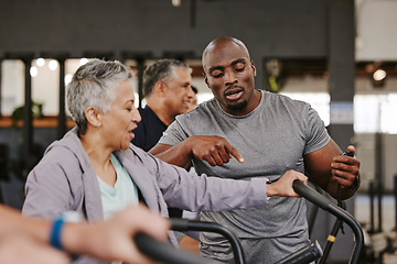 Image showing Elderly group, exercise bike and personal trainer for fitness, timer and retirement wellness by blurred background. Senior woman, bicycle training and diversity with black man, progress and coaching
