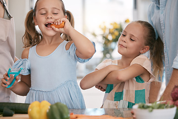 Image showing Children, cooking and a girl eating a carrot in the kitchen while preparing a healthy meal with her family. Kids, food and nutrition with a female child sister biting a vegetable in her home