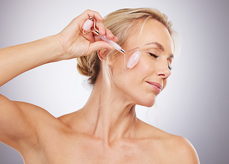 Image showing Woman, roller and skincare for cosmetics, anti aging or facial treatment against a gray studio background. Happy mature female model with rolling tool for beauty aesthetic, wellness or dermatology