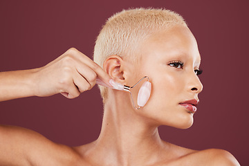 Image showing Face skincare, jade roller and woman in studio isolated on a red background for dermatology. Beauty, cosmetics and female model with product or rose quartz stone for facial treatment and healthy skin