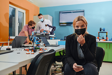 Image showing A woman wearing a protective mask standing in a laboratory while her colleagues test a new robotic invention in the background.