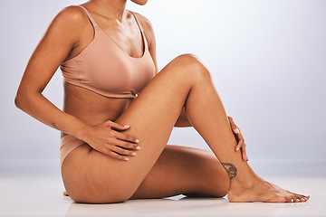 Image showing Hands, legs and skincare with a black woman in studio, sitting on the floor against a gray background for beauty. Fitness, body and tattoo with a female posing for hair removel, wax or laser