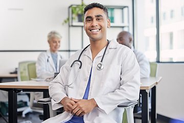 Image showing Young doctor, man and portrait at hospital desk with smile for healthcare, planning and teamwork. Professional leader, doctors and expert in health, wellness and happy in clinic with group at table