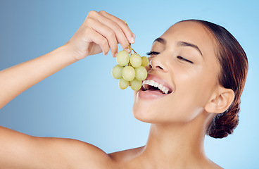 Image showing Skincare, grapes and woman in studio for wellness, detox or organic treatment on blue background. Fruit, snack and girl model with relax during beauty, routine and happy with raw product isolated