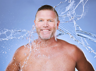 Image showing Portrait, water splash and mature man in studio for cleaning, hygiene and wellness on a blue background. Skincare, face and body care for aging skin of male model in luxury, pamper or beauty routine