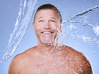 Image showing Showering, water splash and man with smile, cleaning and daily hygiene on blue studio background. Mature male, gentleman and clear liquid for washing, dermatology and skincare for grooming on backdro