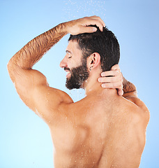 Image showing Hair, washing and man in studio for skincare, grooming and hygiene against blue background. Haircare, body care and guy model relax in shower, happy and isolated on water splash, cosmetic or wellness