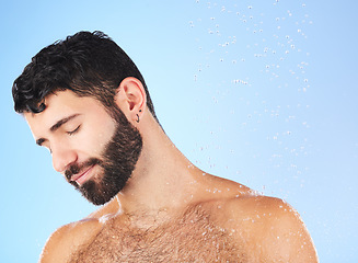 Image showing Man, water drop and shower for hygiene, self care and cleaning on a blue background in studio. face of a aesthetic model person for skincare health and wellness with splash for dermatology cosmetics